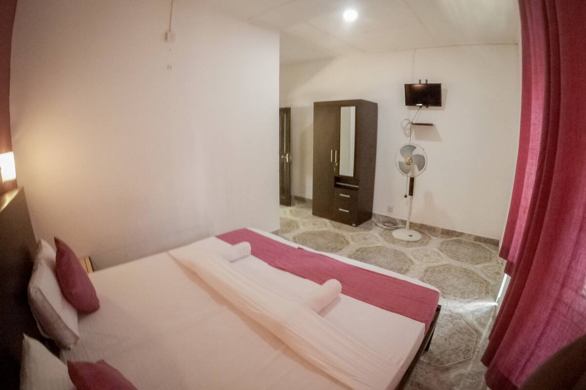 Quarto com cama, espelho, ventoinha e guarda-roupa.