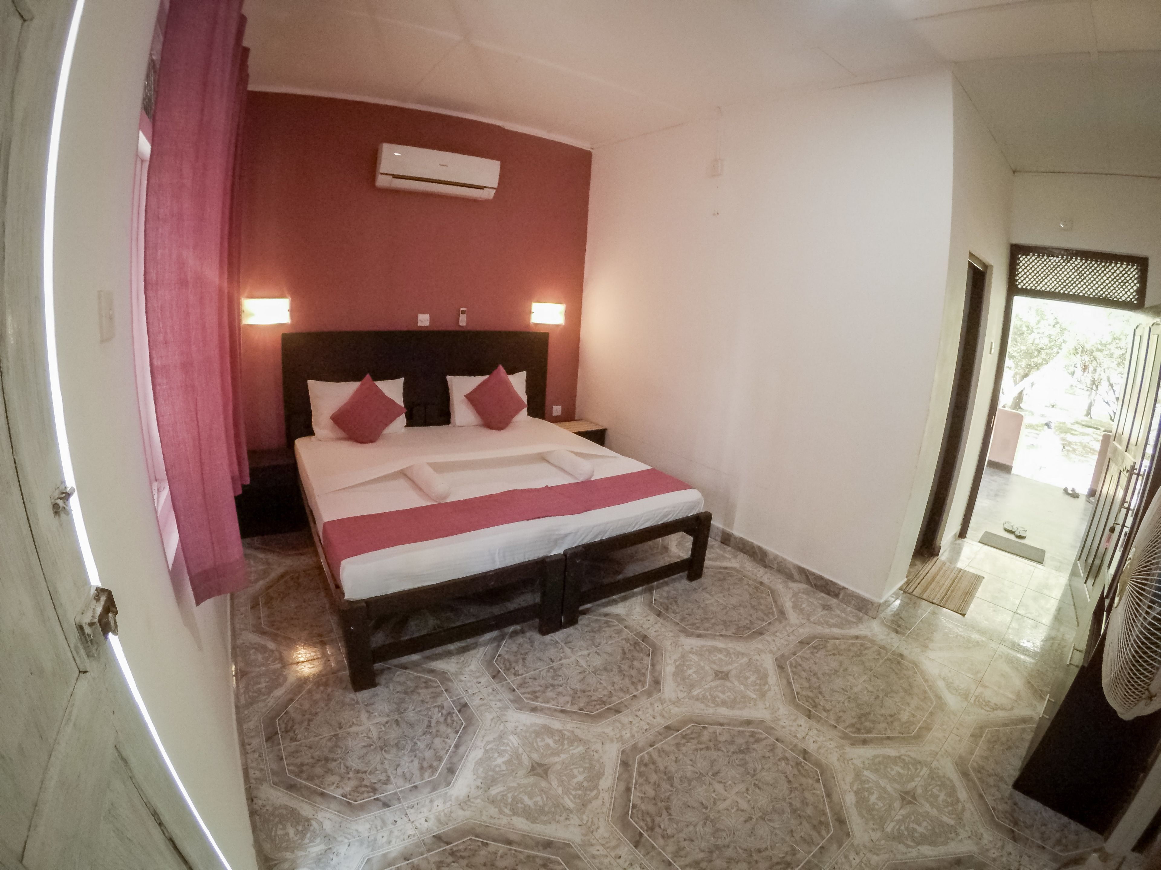 A hotel room with a bed, a headboard, an air conditioning unit, and a tiled floor.