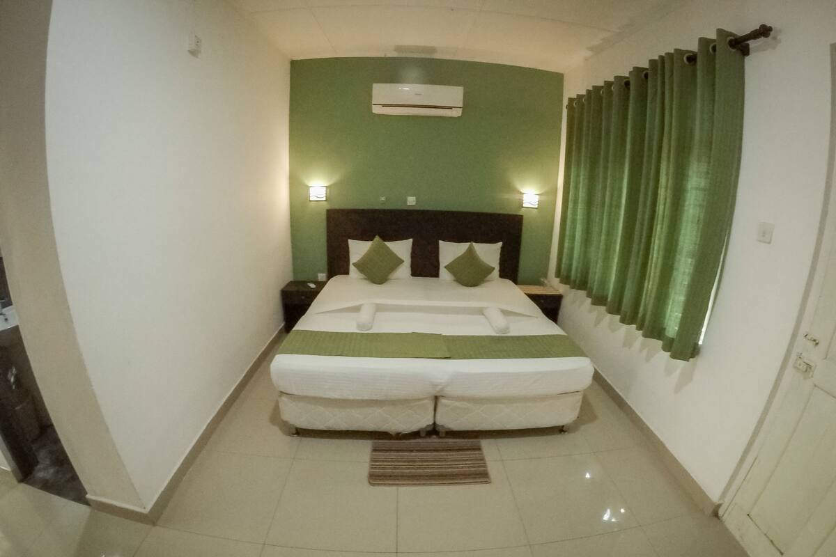 Um quarto com uma cama grande, paredes verdes e uma janela com cortinas verdes.