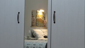 Quarto com cama, mesa de cabeceira e prateleira fixada na parede com objetos decorativos.