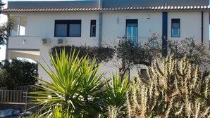 Um edifício de dois andares com telhado plano, paredes brancas e varanda no segundo pavimento.