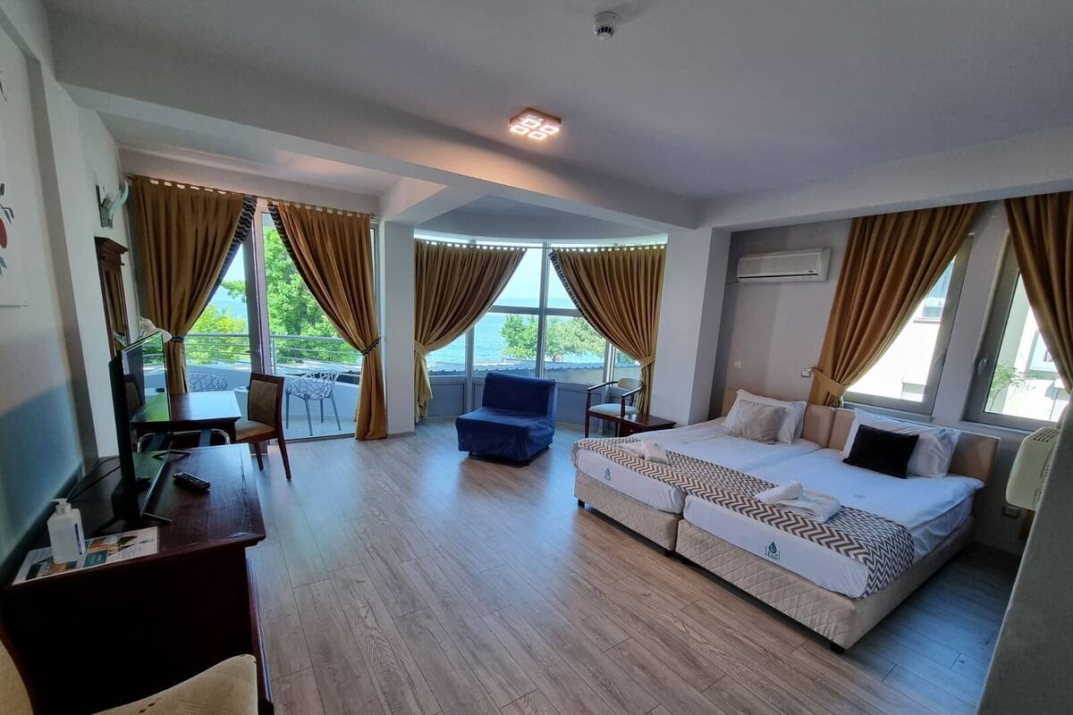A hotel room with a large bed, a desk, a chair, and a balcony with curtains.