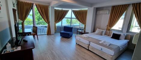 A hotel room with a large bed, a desk, a chair, and a balcony with curtains.