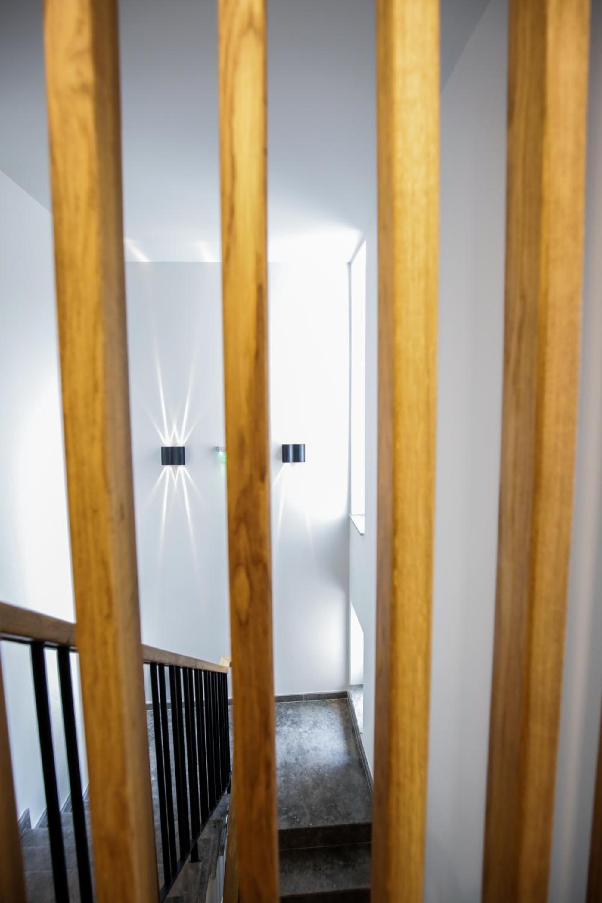 A staircase with wooden railings and a modern light fixture on the wall.