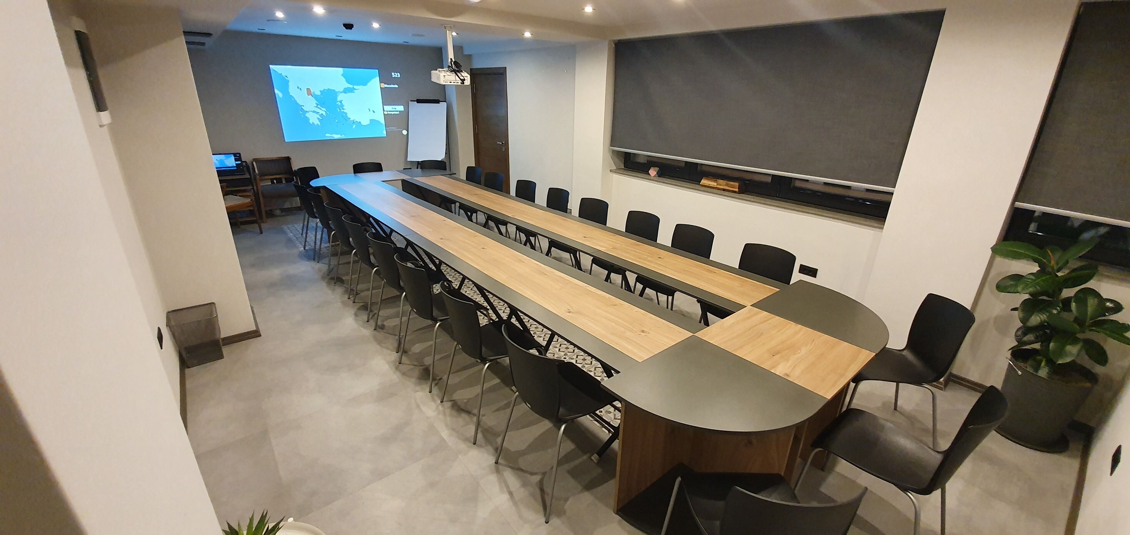 A conference room with a long table, black chairs, a projector screen, and a whiteboard.