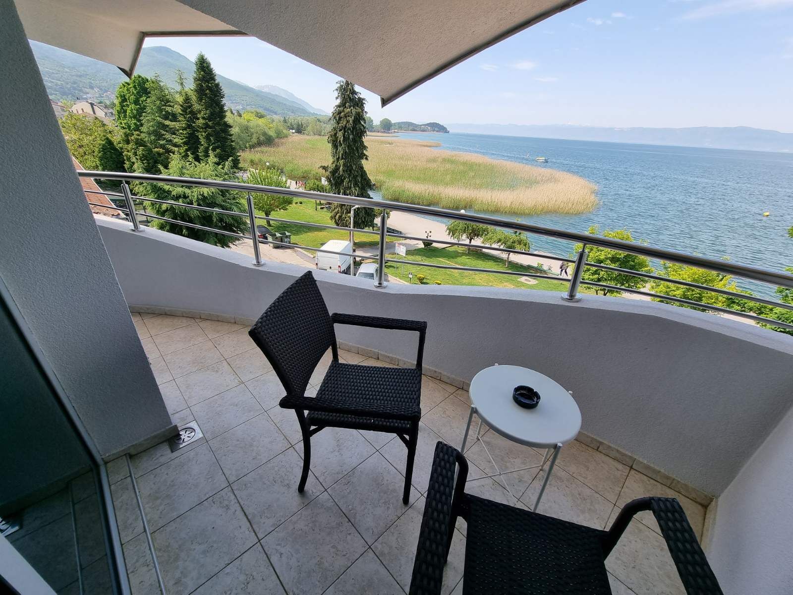 A balcony with a view of a lake, a chair, and a small table.