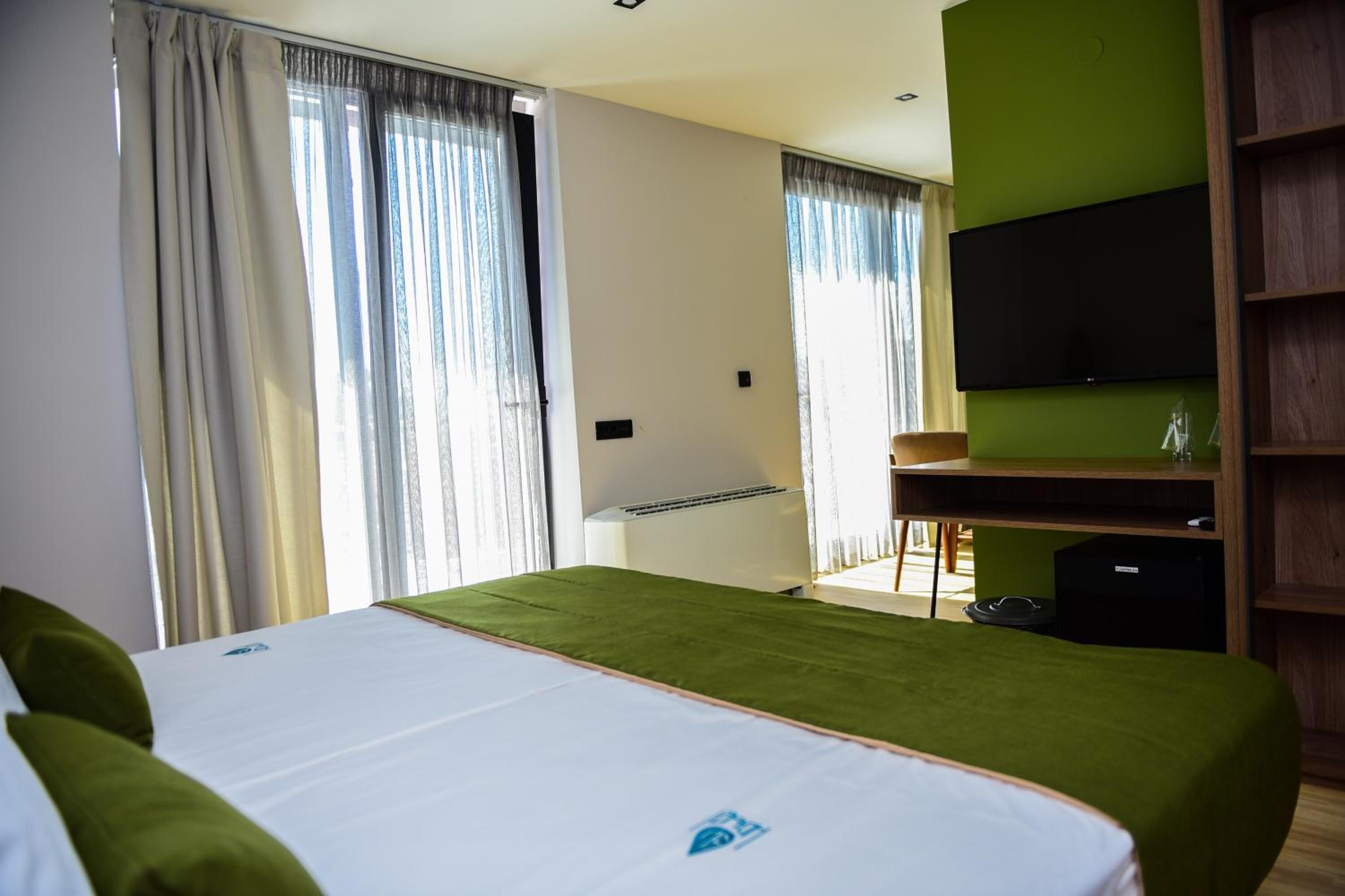 Una camera d'albergo con un letto, una scrivania, una televisione e una parete verde.