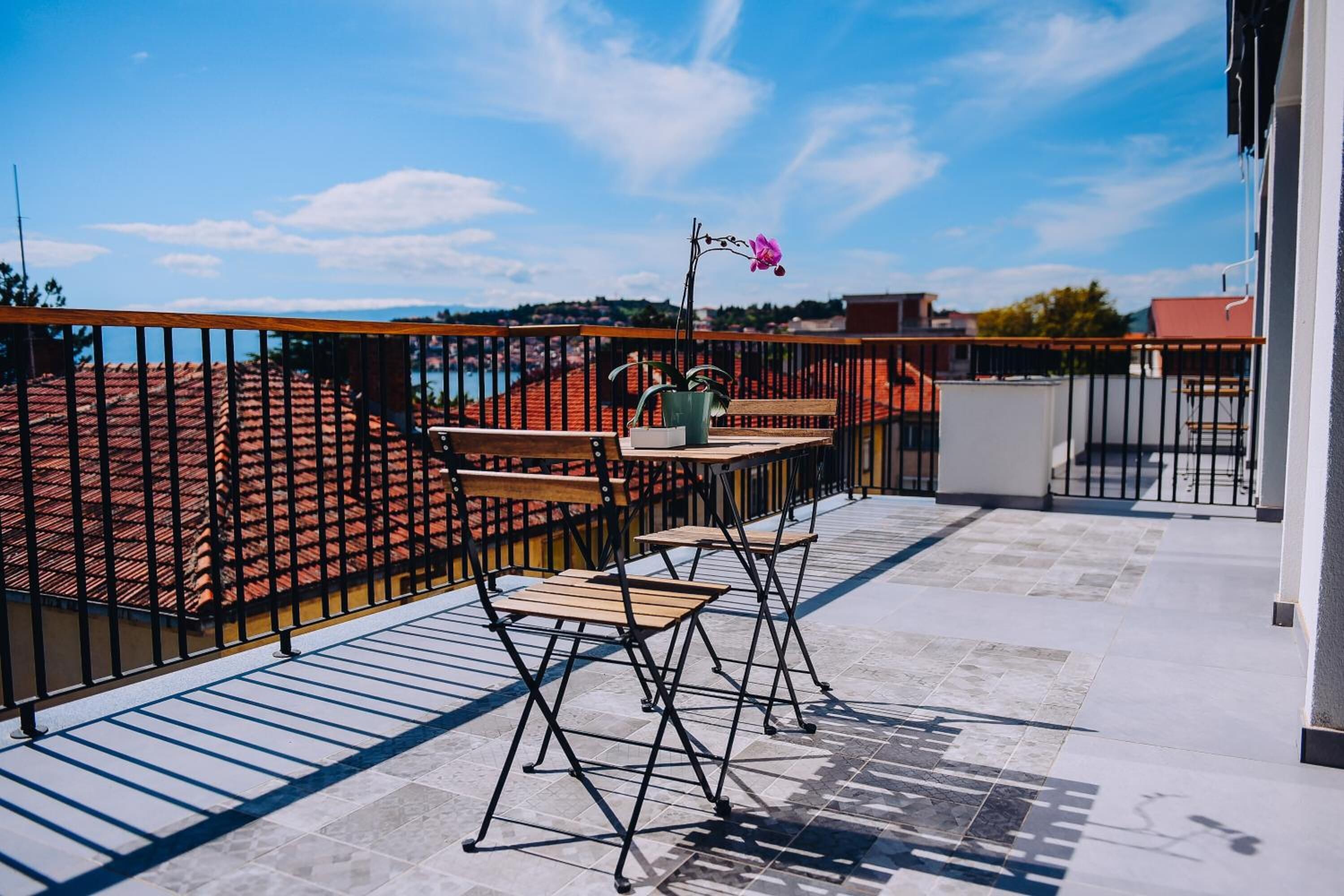 A terrace with a table and chairs, a potted plant, and a view of buildings and a body of water.