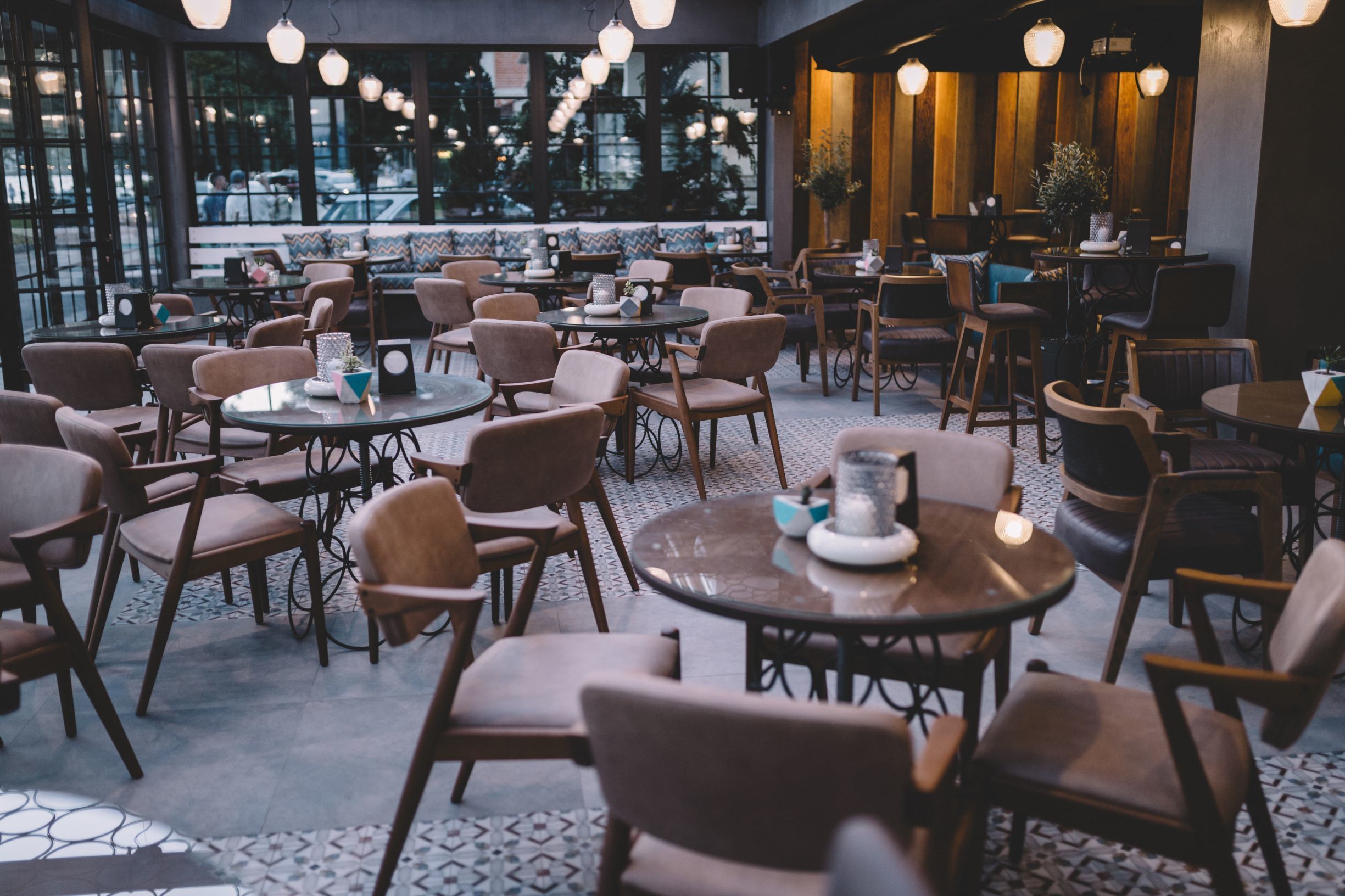 Un espace intérieur spacieux avec des tables et des chaises rondes, de grandes fenêtres donnant sur la rue et un éclairage chaleureux.