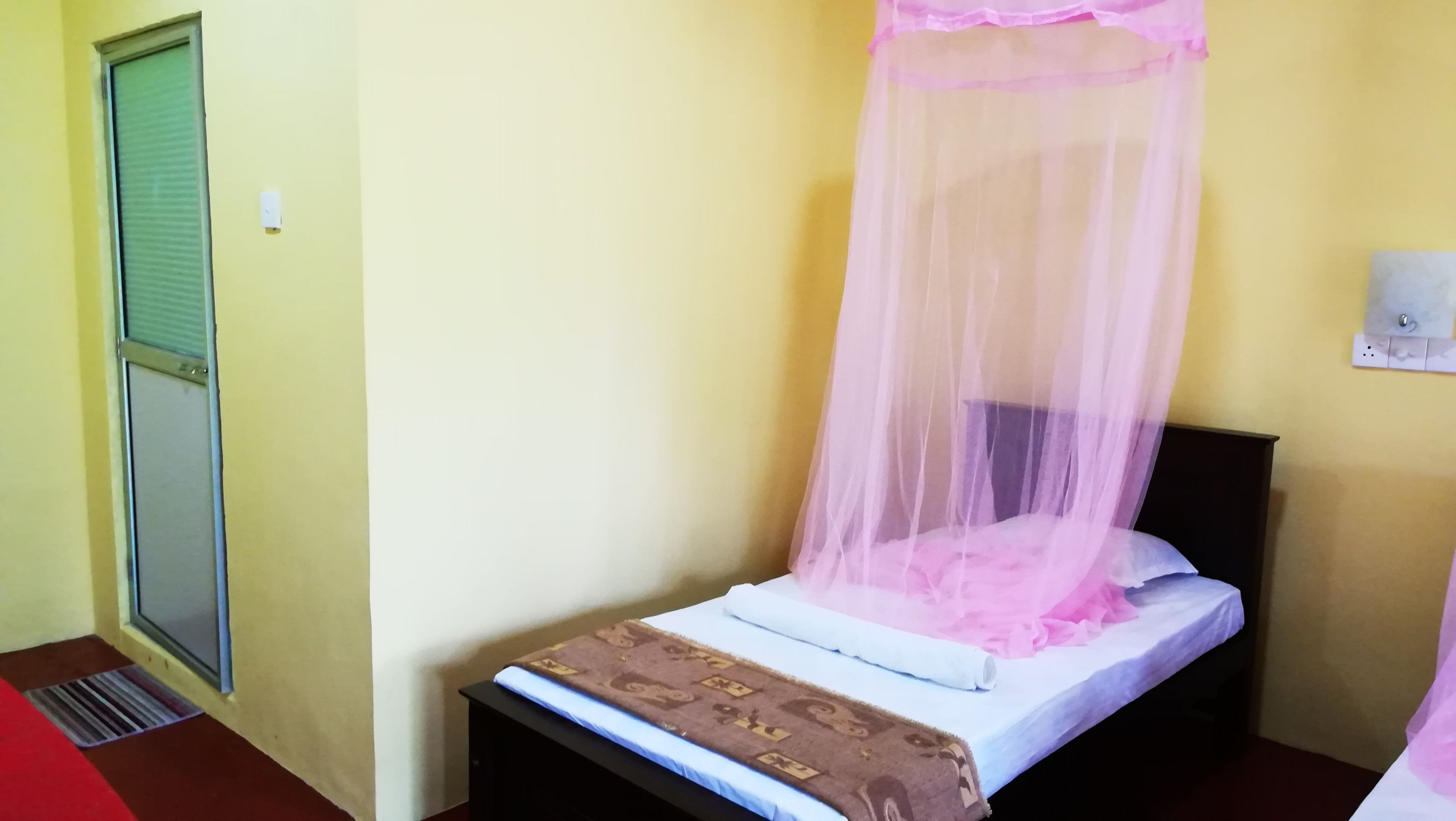Un lit simple avec un baldaquin, une table de chevet et une prise électrique murale.