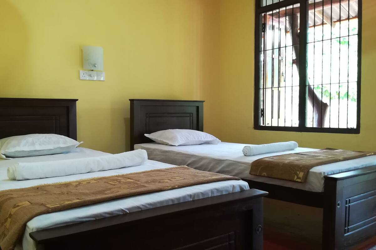 A room with two beds, each with white linens and a brown blanket. There is a wall-mounted light fixture above the beds.