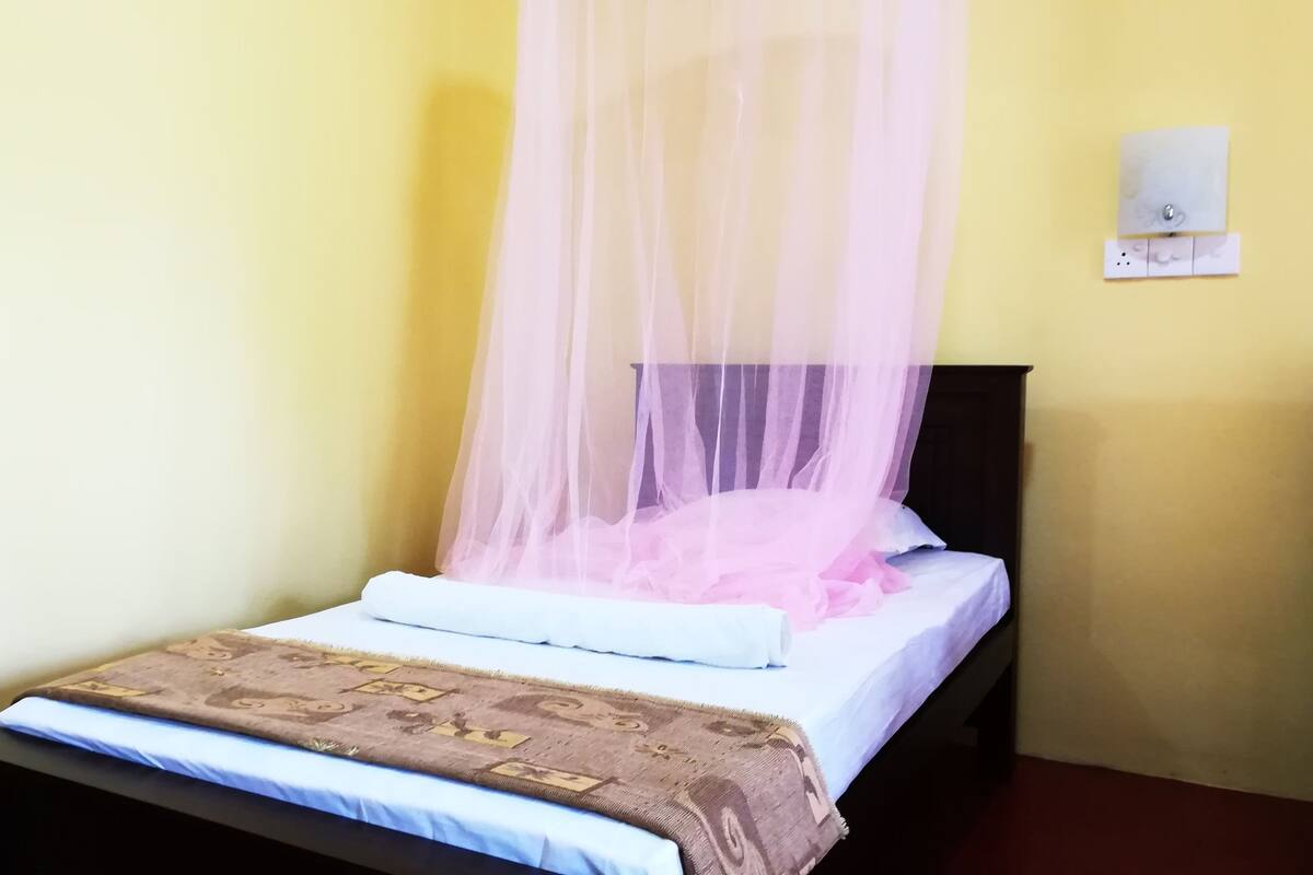 A single bed with a mosquito net, a bedside table, and a wall socket.