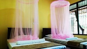 Duas camas com mosquiteiros, uma janela com grades e uma parede amarela.