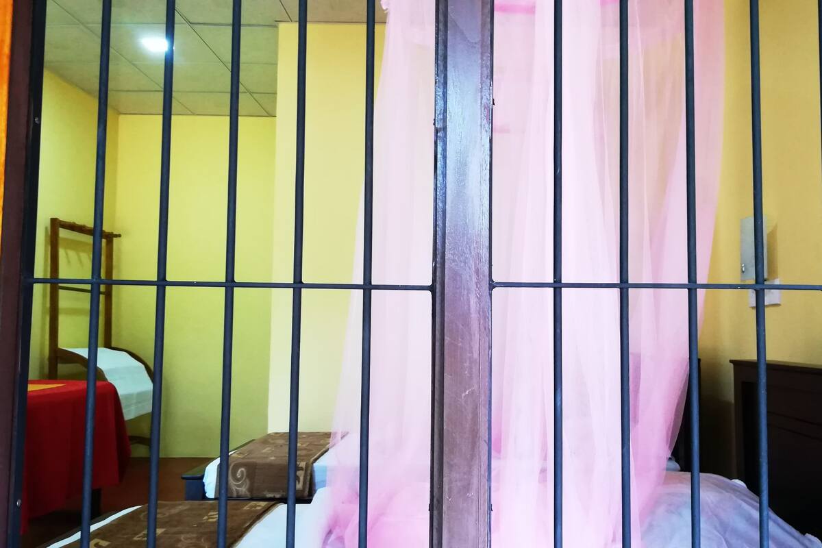 A room with a bed, a table, and a chair, separated by a metal partition.