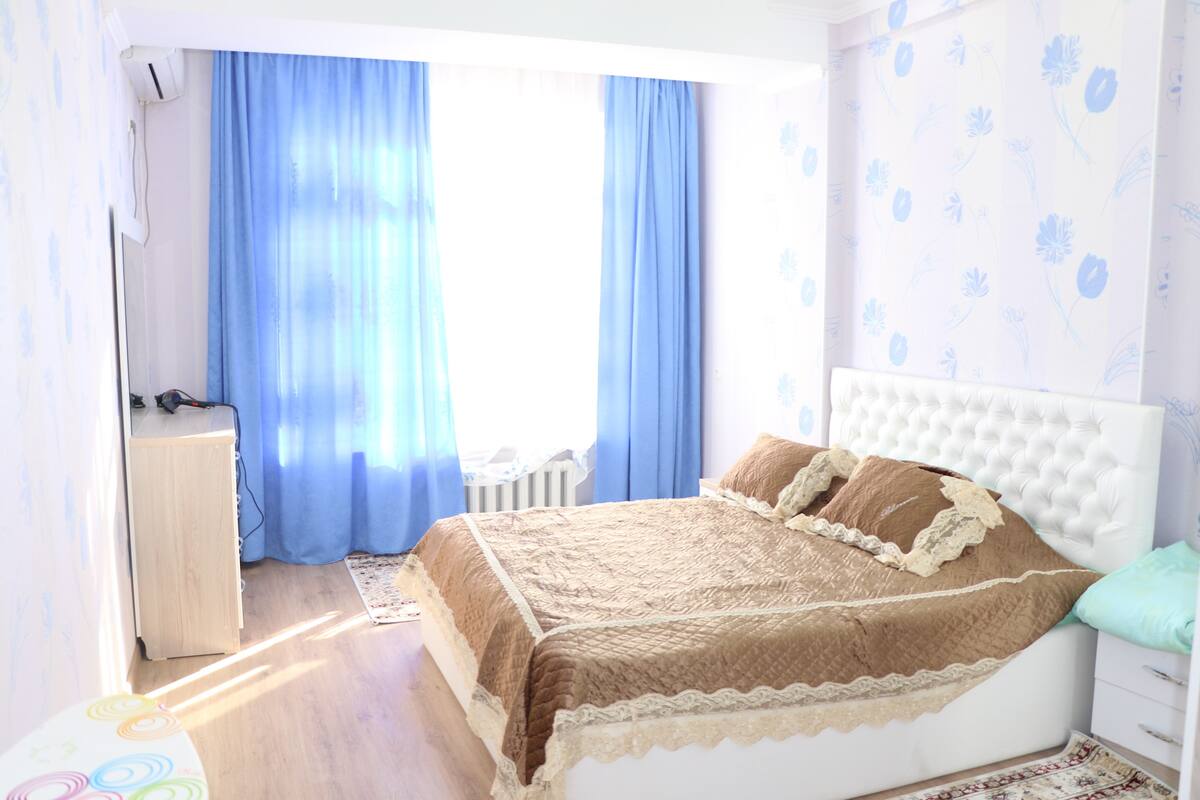 Een slaapkamer met een bed, gordijnen, een radiator en een radiatoromsluiting.