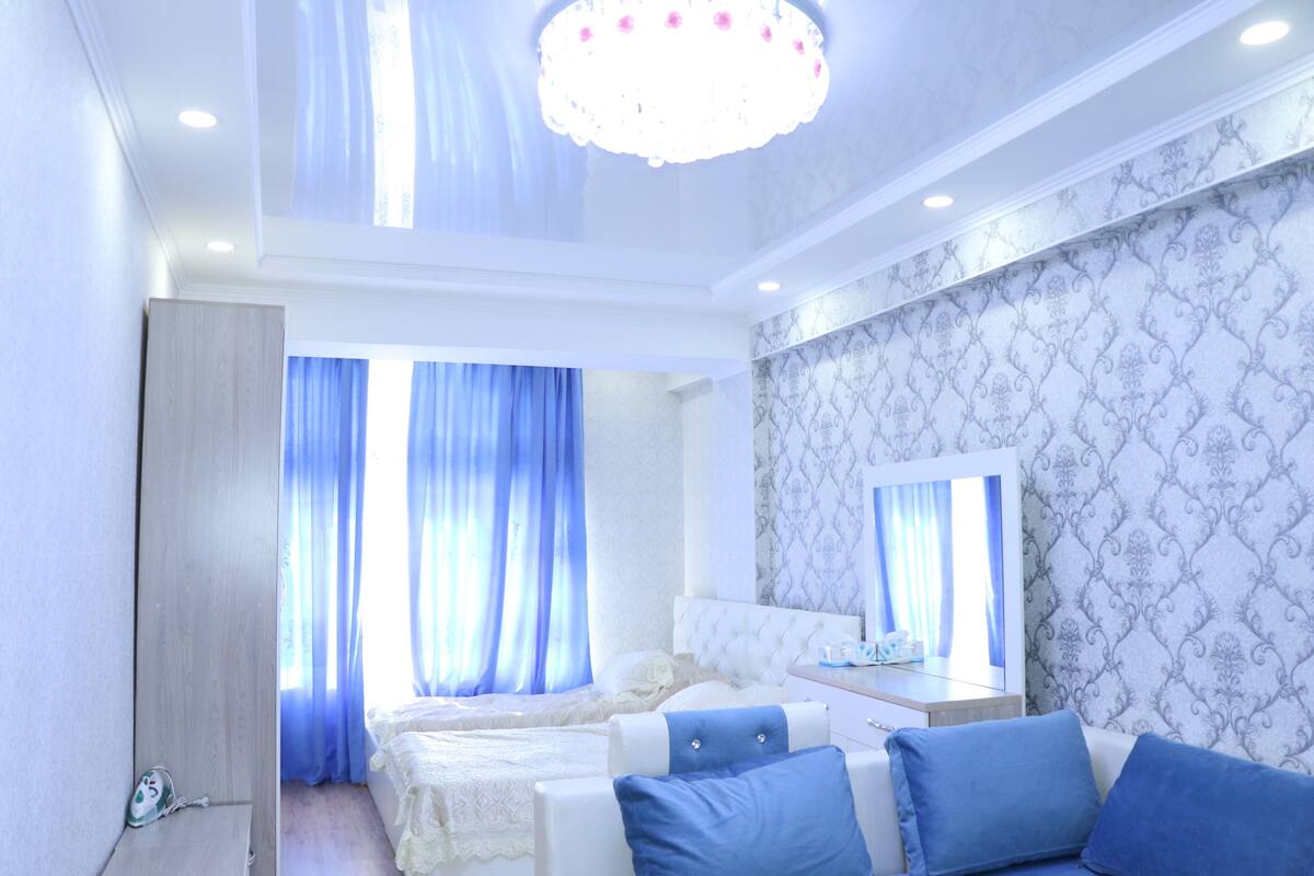 Een slaapkamer met een bed, nachtkastje, spiegel en een raam met gordijnen.
