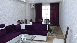 Ein Wohnzimmer mit einem violetten Sofa, einem Glastisch und einem Essbereich mit Tisch und Stühlen.