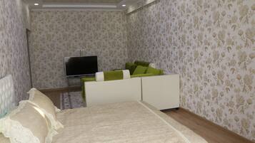 A bedroom with a bed, a TV, and a sofa with green cushions.