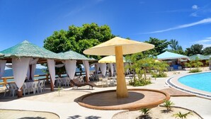 Zona de piscina en un resort con sombrillas de paja, sillas de descanso y una terraza de madera.