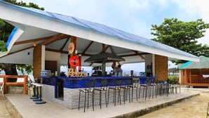 Un bar frente a la playa con mostrador de azulejos, zona de estar y un letrero de Coca-Cola.