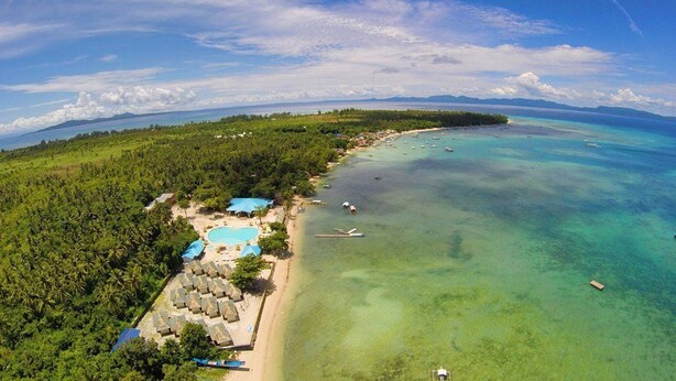 Vista aérea de un resort tropical con playa, aguas cristalinas y exuberante vegetación.