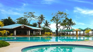 Zona de piscina con un edificio, palmeras y cielo despejado.