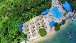 Vista aérea de un resort con piscina, playa y exuberante vegetación.