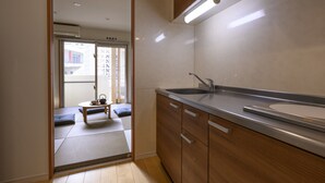 A kitchen with wooden cabinets, a stainless steel sink, and a sliding door leading to a balcony. - TOKI NO YADO NAHA by SUNREST RESORT (Naha)