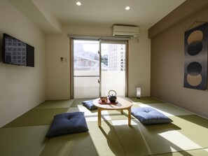 A traditional Japanese room with tatami flooring, a low wooden table, cushions, and a sliding door leading to an outdoor area.