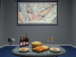 A room with a projector screen displaying a sports image, a table with snacks, drinks, and a basket.