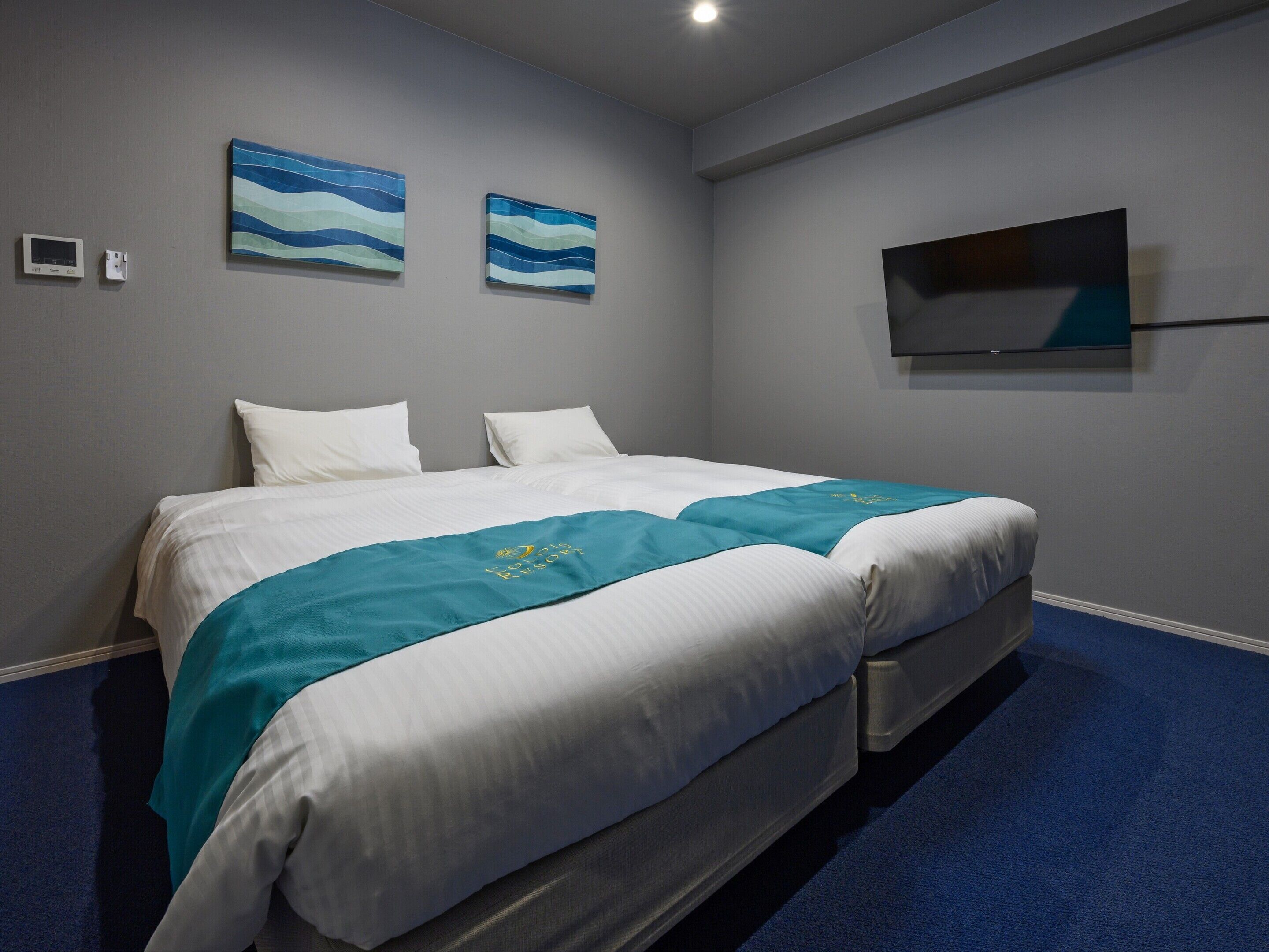 A hotel room with a bed, two wall-mounted TVs, and a blue carpet.