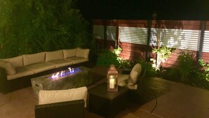 Ein Außenbereich mit Terrasse, einer Sitzecke, einem Couchtisch mit integriertem Feuerkorb, einer Laterne und einem kleinen Tisch.