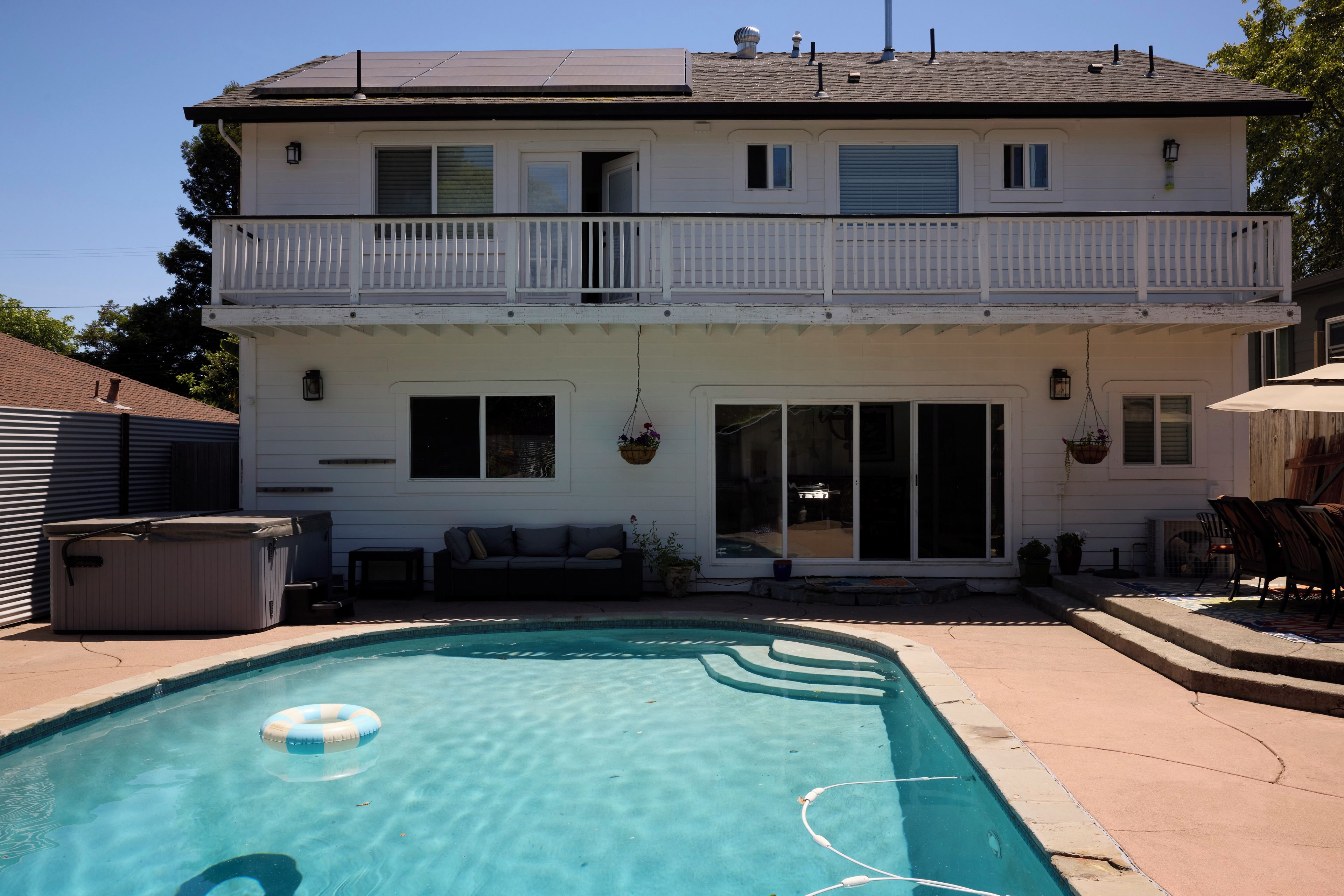 A two-story house with a backyard swimming pool, a hot tub, and outdoor furniture.