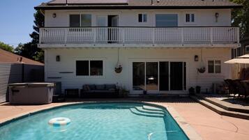 A two-story house with a backyard swimming pool, a hot tub, and outdoor furniture.