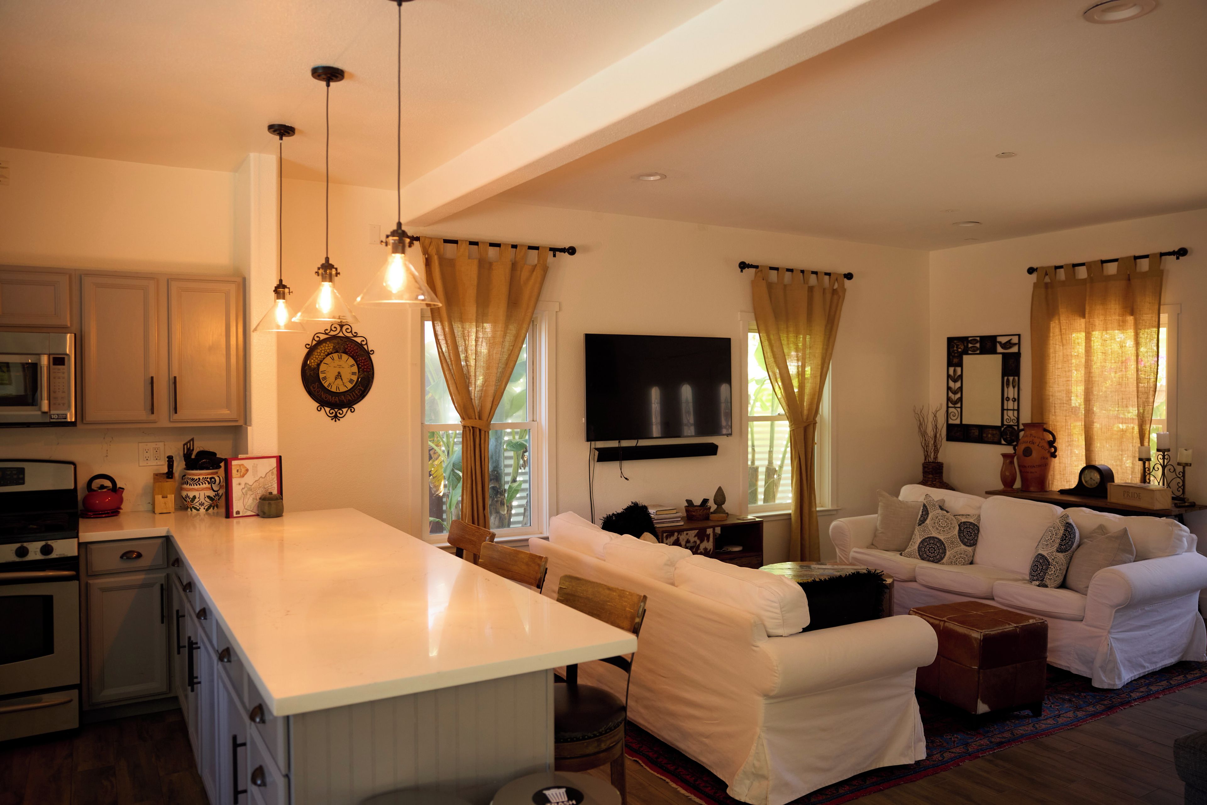 Cozinha moderna com ilha central, área de jantar com sofá e mesa, e sala de estar com televisão e objetos decorativos.