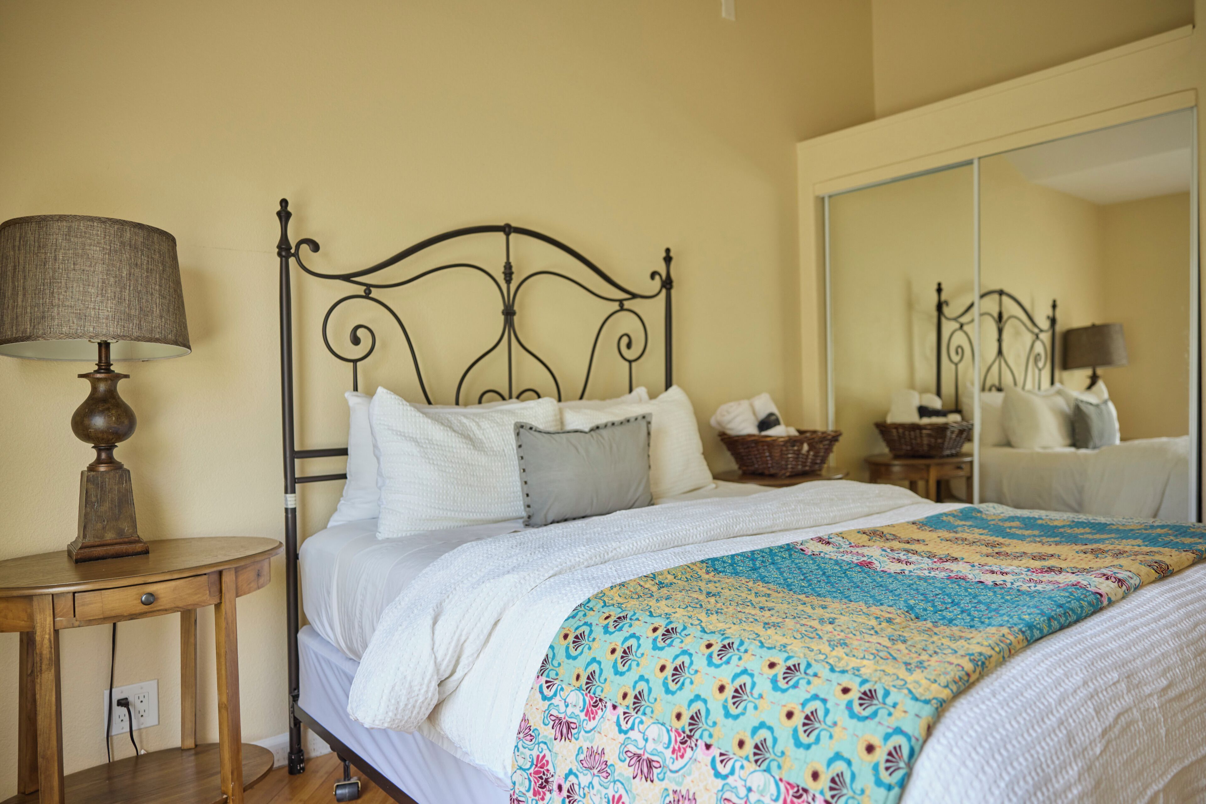 A neatly made bed with a patterned blanket, a bedside lamp, and a mirror on the wall.