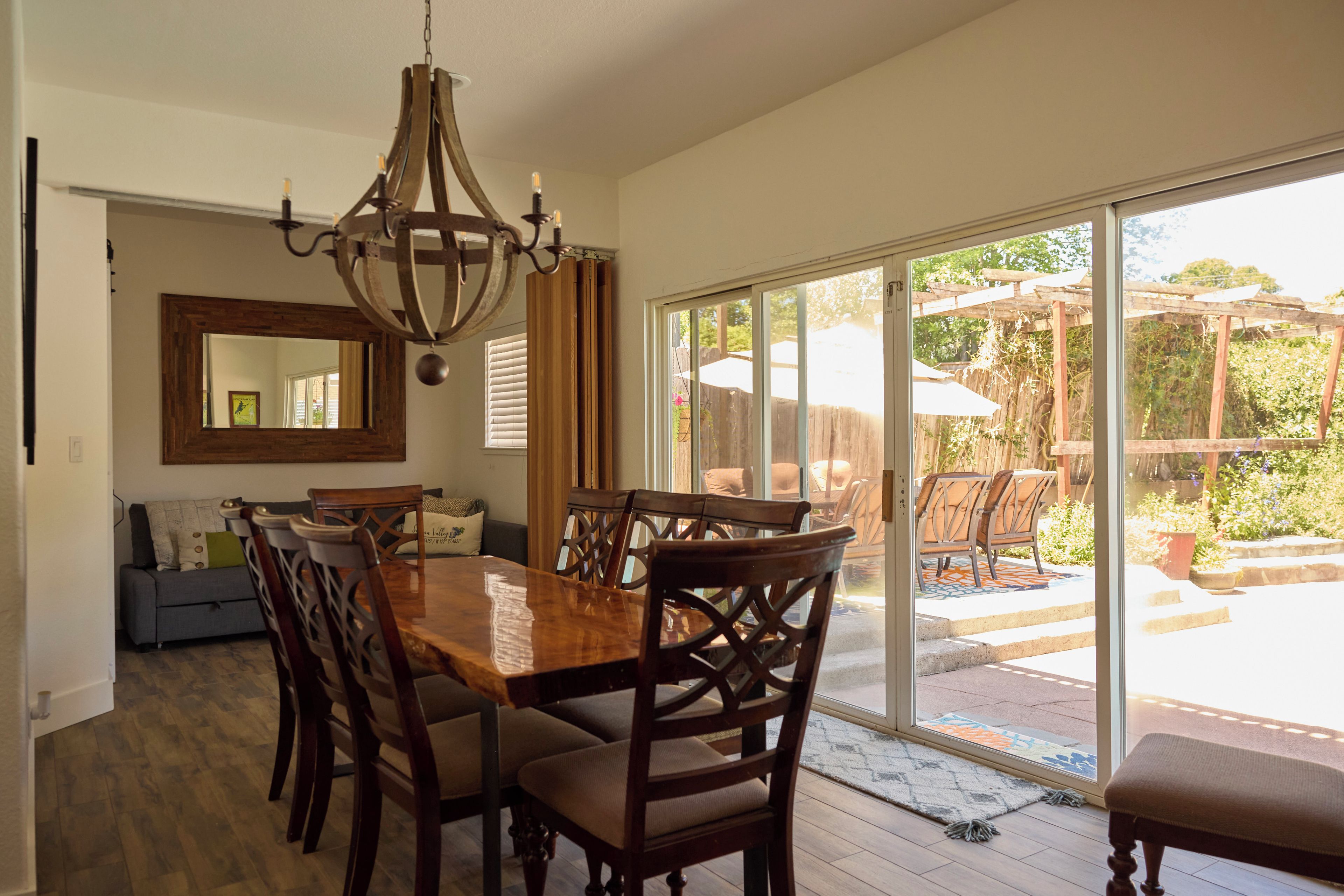 A dining area with a large wooden table, chairs, a chandelier, and a sliding glass door leading to an outdoor patio.
