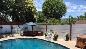 Un jardin avec une piscine, une terrasse en bois, un mur en pierre et un espace détente avec un canapé et un parasol.