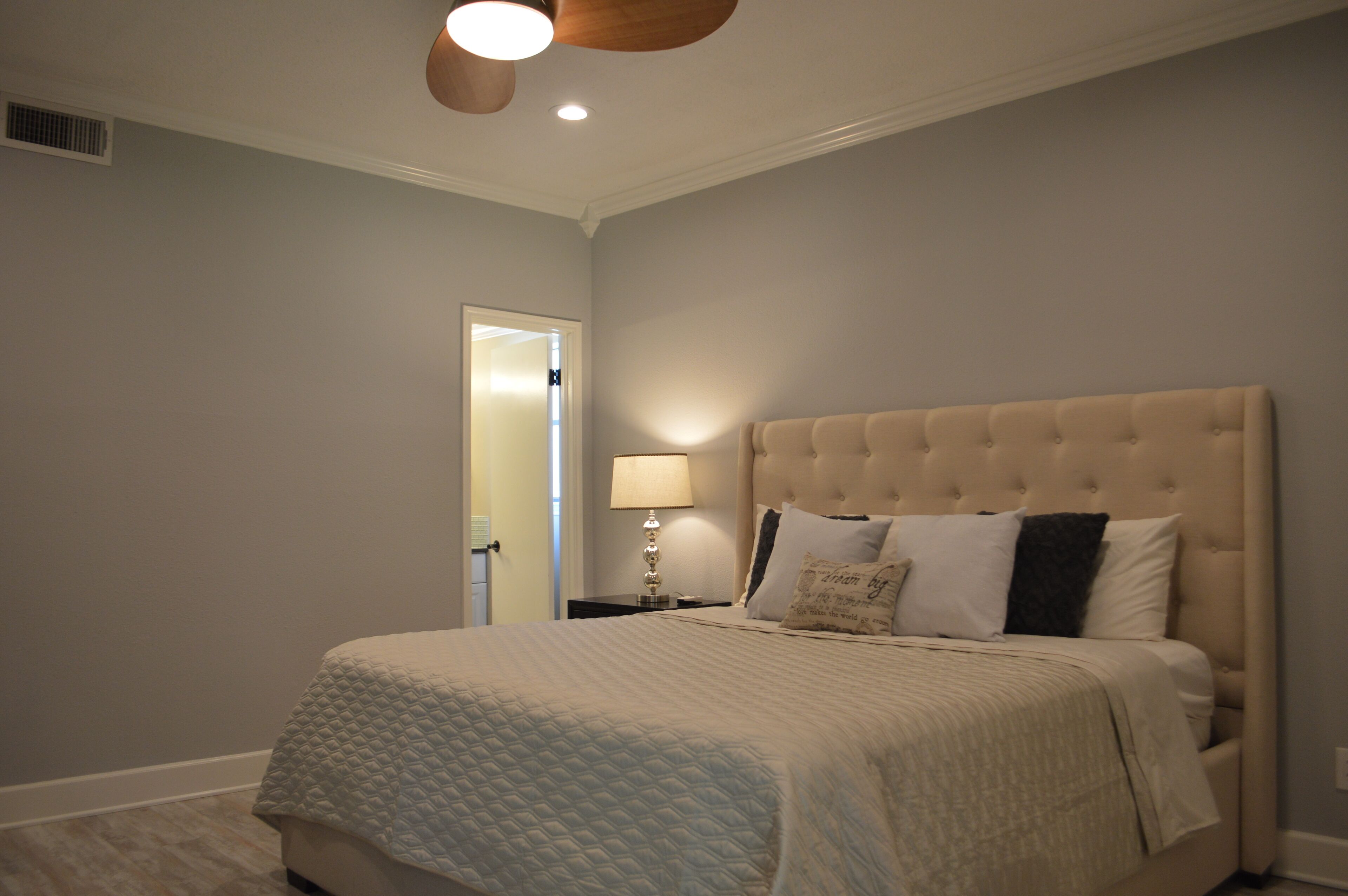 Camera da letto con un letto grande, un comodino con una lampada e una porta che dà su un'altra stanza.