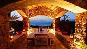 An outdoor dining area with stone walls, a wooden table, and lanterns. - Villa Hurmuses (Mykonos)