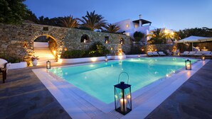 A swimming pool with stone walls and archways, surrounded by lounge chairs and lanterns. - Villa Hurmuses (Mykonos)