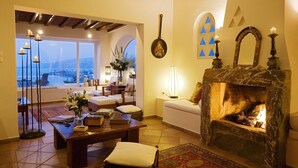 A cozy living room with a fireplace, a sofa, a coffee table, and a view of the sea. - Villa Hurmuses (Mykonos)