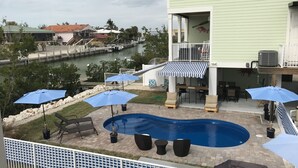 Een zwembad met ligbedden en parasols, uitzicht op een rivier, en een gebouw met een balkon.