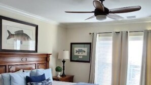 Een slaapkamer met een bed, een stoel, een plafondventilator en een raam met gordijnen.