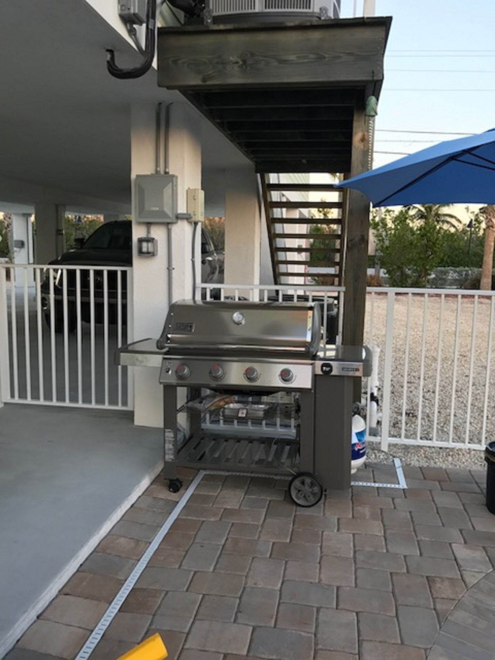 Een barbecue met een schoorsteen, een wit hek en een blauwe parasol op de achtergrond.