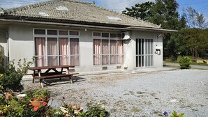 Un edificio con techo de tejas, ventanas grandes y un pequeño espacio exterior con una banca.