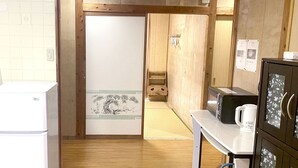 Una cocina con refrigerador, microondas y alacenas. Se ve una puerta de madera que conduce a otra habitación.
