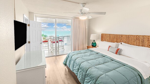 Ein Hotelzimmer mit Bett, Fernseher, Deckenventilator und Meerblick durch eine Schiebetür.