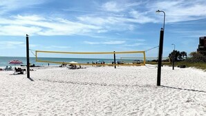 Ein Beachvolleyballfeld mit Netz, umgeben von Sand und Liegestühlen.