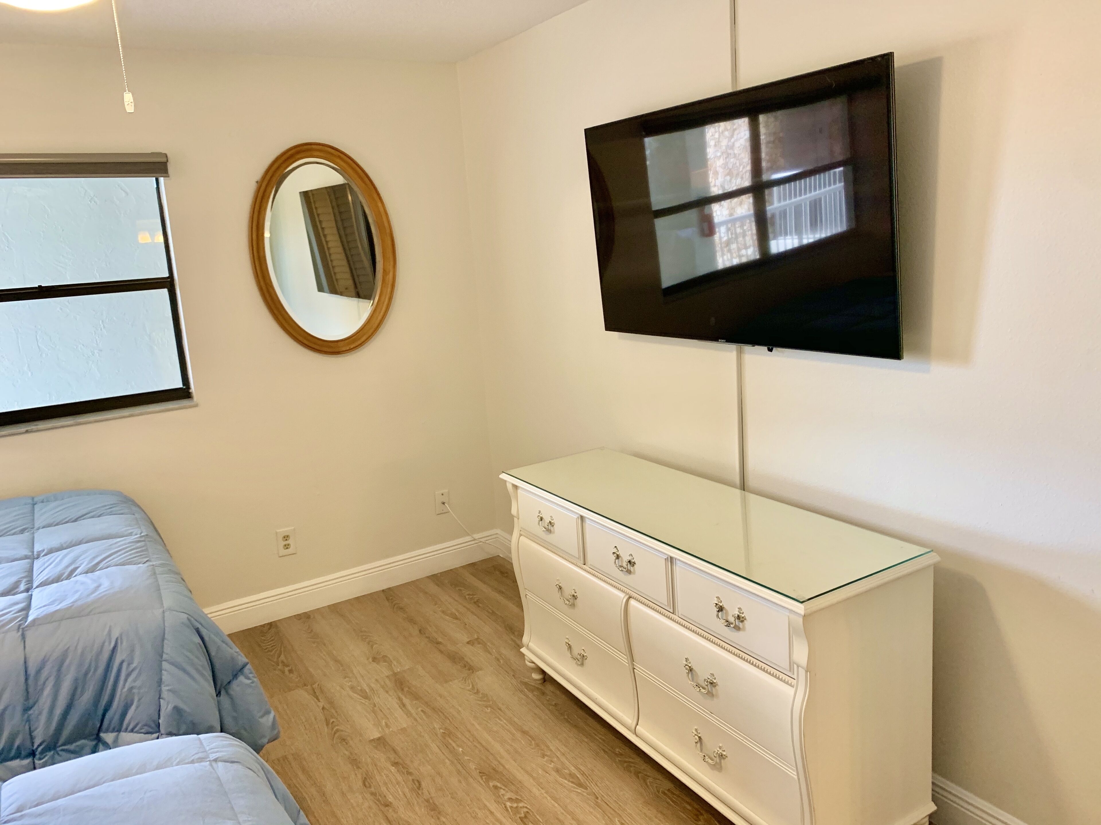 A bedroom with a bed, a dresser, a mirror, and a TV mounted on the wall.